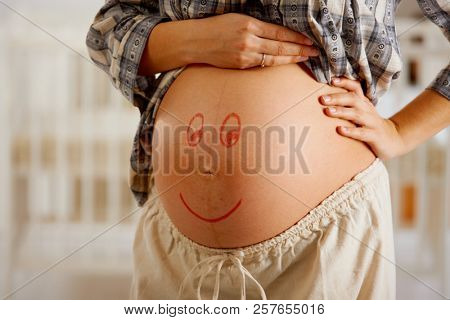 Close-up of pregnant belly with drawn smiley face.