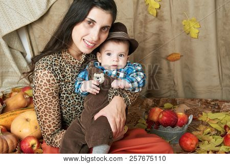 autumn concept - mother and child boy are on yellow leaves with fruits and vegatbles, red apples and pumpkins