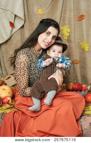 autumn concept - mother and child boy are on yellow leaves with fruits and vegatbles, red apples and pumpkins