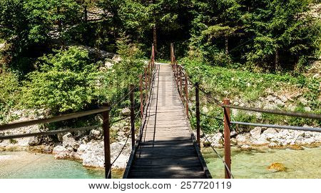 Wooden Hanging Bridge Leading Forward Over Green Mountain River.