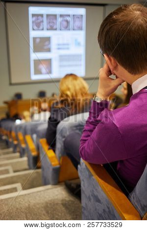 Listeners in auditorium during medical conference, rear view.