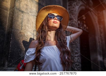 Outdoor Portrait Of Young Tourist Woman Walking On Old City Street. Traveler Girl In Hat Looking At 