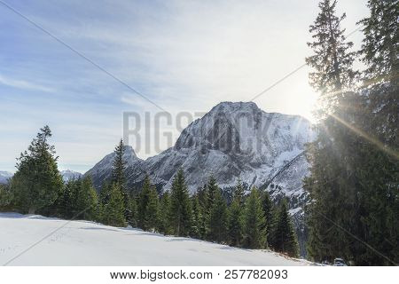 Winter Scenery With The Sun Shining Over The Snowy Austrian Alps, The Green Forest And White Valley,