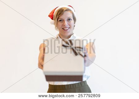 Positive Attractive Saleswoman In Santa Hat Giving Gift To You. Happy Middle-aged Lady Presenting Ch