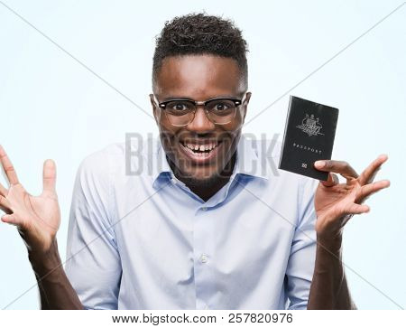Young african american man holding australian passport very happy and excited, winner expression celebrating victory screaming with big smile and raised hands