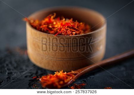 Saffron Spice. Saffron spices on black stone table in a wood bowl and a spoon. Spice and herbs on slate background. Seasonings, condiments. Cooking ingredients, flavor
