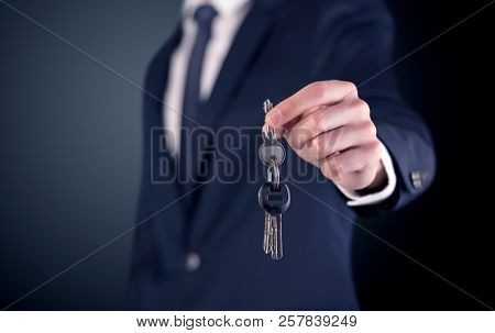 Young businessman hand over keys with empty dark background