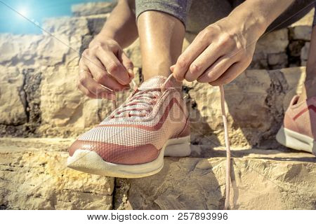 Women runner bootlace on her boot after running in sunny day under sunlight from blue sky on the stone steps.