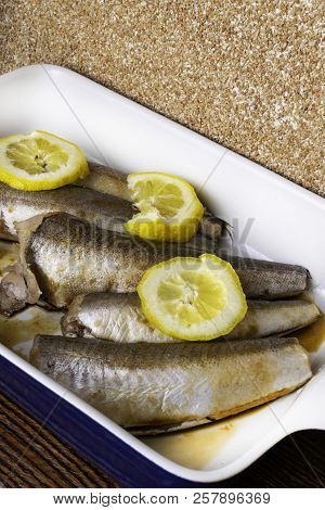 Raw Fish Hake With Lemon Slices, Spices, Olive Oil On White Pan