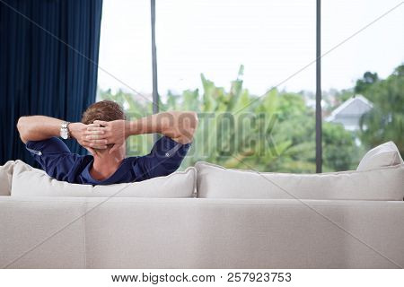 Portrait Of Young Man With Hands Behind His Head Is Relaxing On Couch