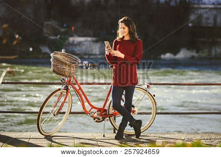 Theme Tourism On Bicycle And Modern Technology. Beautiful Young Caucasian Woman Stands Near Red Retr