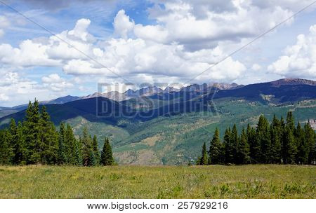 Colorado Landscape From The Top Of Vail Mountain, Showing Pine Trees, Wild Grass, And Mountains With