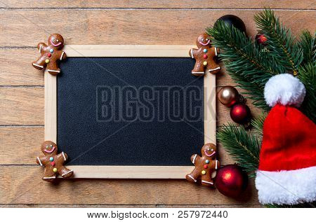 Gingerbread Man With Christmas Decoration And Blackboard On Wooden Table. Above View In Old Color St