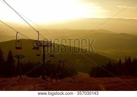 People Walks Under Ski Chair Lift In The Jeseniky Mountains At Sunset.