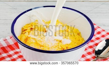 Breakfast With Cornflakes. Pour Milk Into A Bowl With Corn Flakes. The Yogurt Splashes Out Into Corn