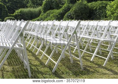 View Of Empty Wooden Chairs In White, Arranged In Rows On The Lawn, Against The Background Of Park P