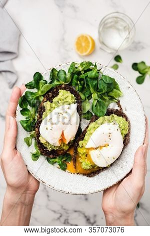 Avocado And Poached Egg On Rye Bread. Female Hands Holding Healthy Vegetarian Breakfast Or Snack Rye