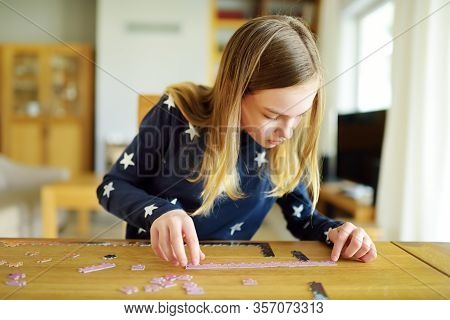 Cute Young Girl Playing Puzzles At Home. Child Connecting Jigsaw Puzzle Pieces In A Living Room Tabl