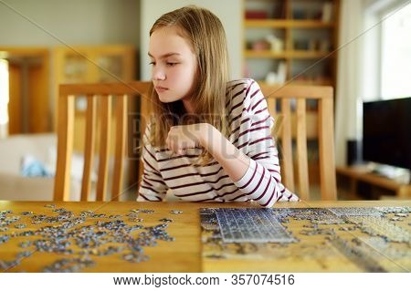 Cute Young Girl Playing Puzzles At Home. Child Connecting Jigsaw Puzzle Pieces In A Living Room Tabl