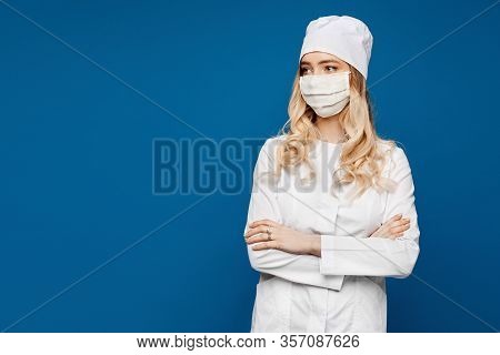Young Nurse In A White Medical Gown And Medical Mask On A Blue Background, Isolated. Female Doctor I
