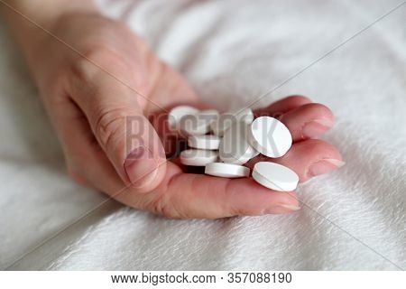 White Pills In A Palm Of Female Hand On The Bed. Concept Of Medication, Vitamins Or Sleeping Pill