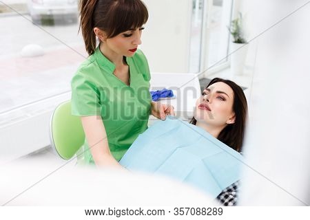 Dentist Doctor Puts Dental Napkin On Patient. Preparing The Patient For A Dental Examination