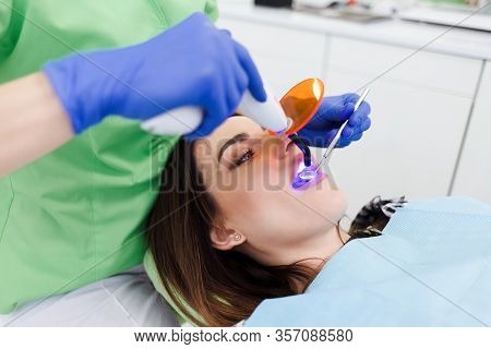 Girl Treats Teeth At The Dentistry. Dentist Using Dental Curing Uv Lamp On Teeth Of Patient
