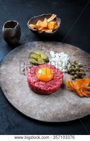 Gourmet tartar raw from beef fillet with yellow of the egg and gherkin with capers and onion rings as closeup on modern design plate 