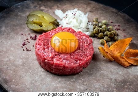 Gourmet tartar raw from beef fillet with yellow of the egg and gherkin with capers and onion as closeup on modern design plate 