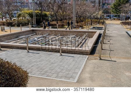 Daejeon, South Korea; March 16, 2020: Unidentified People Walking Past Dry Water Fountain In City Pa
