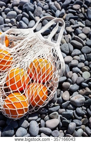 White Cotton Eco String Bag With Oranges On A Rocky Beach. Zero And Eco Waste. No Plastic. Bright Ba