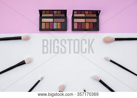 Top View Of Colorful Metallized Eyeshadow Pallete And Natural Makeup Brushes Set On White And Pink B