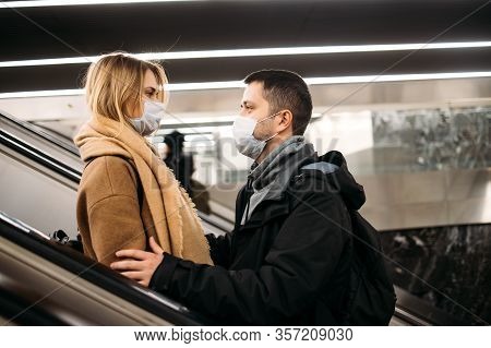 Side View Of Young Couple In Medical Masks On Escalator In Subway. Coronavirus Pandemic.
