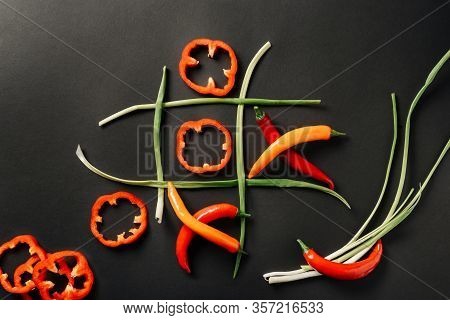Tic-tac-toe With Slices Of Bell Pepper And Hot Pepper, On A Black Surface With Leek.