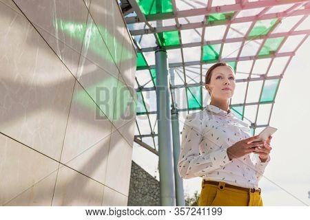 Low angle view of young attractive businesswoman standing while using smartphone