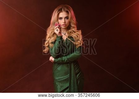 Blonde Woman, Bright Make-up, Green Stylish Dress And Jewelry. Showing Two Red Chips, Propping Her E