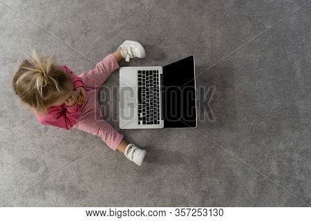 Small Cute Blond Caucasian Baby Laying On Floor On Grey Rug And Watching Cartoons On Laptop With Gre