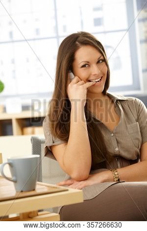 Stay at home - Young woman talking on mobilephone with an impish smile biting her little finger.