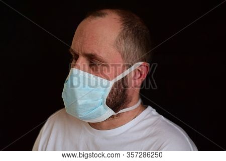 Man In A Medical Mask On A Black Background. Portrait, Close-up. Bokeh. Selective Focus.