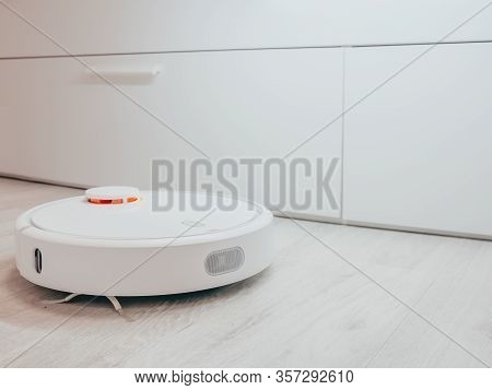 White Robot Vacuum Cleaner On A Laminate On A White Bed Background.