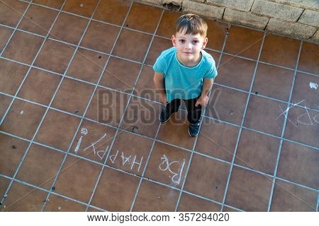 Little Boy Wrote On The Road, Be Happy. View From Above. Cute Boy Drawing With A Chalk.