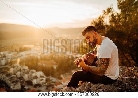 Young Guitarist Playing Acoustic Guitar And Looking To Sunset.searching Inspiration.music Creator.ne