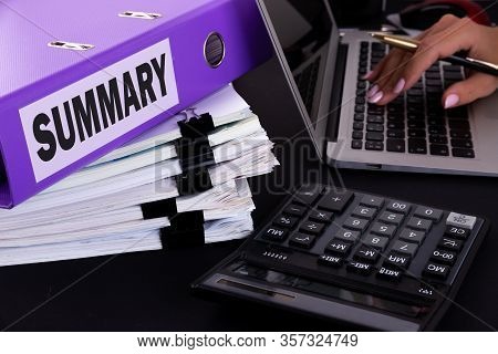 Folder With The Text Summary Written On It Lies On A Dark Office Desk With A Laptop, Hand With Pen, 