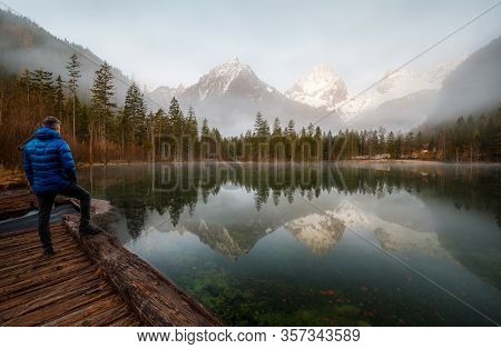 Man Standing At A Mountain Lake Enjoying The Sunrise In The Austrian Alps