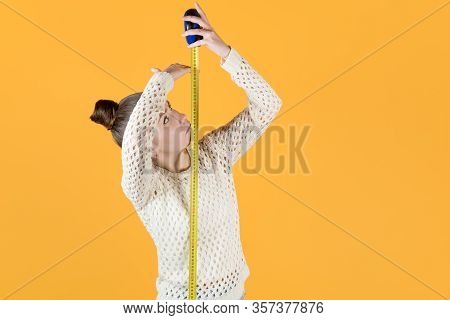 Girl Puzzled Measures Her Height, Holding A Measuring Tape Nearby, Isolated On Orange-yellow
