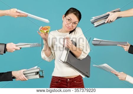 Smiling Office Employee Holds The Phone With Her Shoulder, Drinks Coffee, Eats A Sandwich And At The