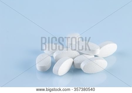 Heap Of White Medical Pills On A Light Blue Background. Pharmaceutical Medicament, Cure For Health. 
