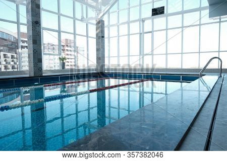 Indoor swimming pool with panoramic windows overlooking city buildings
