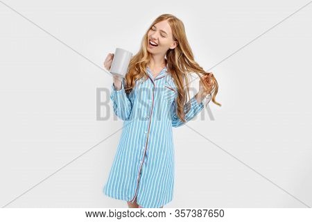 Beautiful Girl In Striped Pajamas, With A Cup In Her Hands , Drinking Coffee Or Tea In The Early Mor