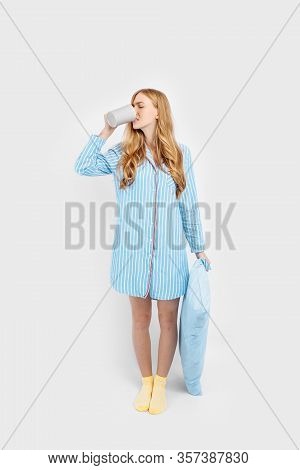 Beautiful Girl In Striped Pajamas, With A Cup In Her Hands , Drinking Coffee Or Tea In The Early Mor